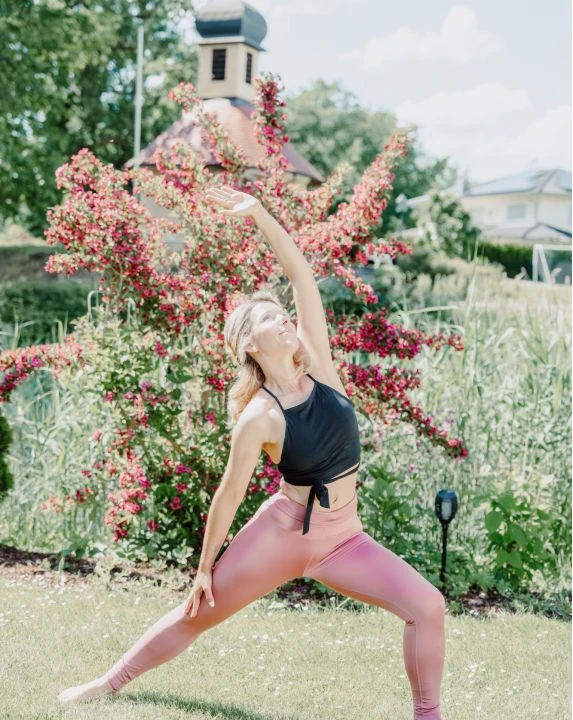 Wie kann man Stress abbauen? 1 Frau bei Yoga im Garten mit der Eisvogel Kappelle im Hintergrund