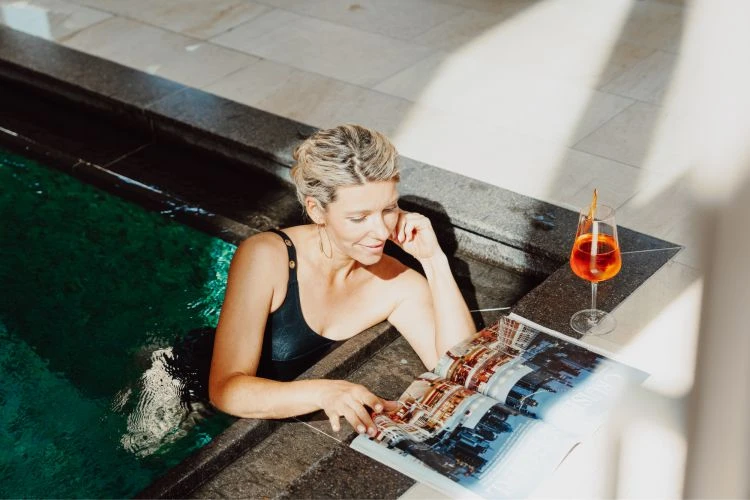 Last Minute Deals 13 Frau am Poolrand mit Zeitung und Getränk
