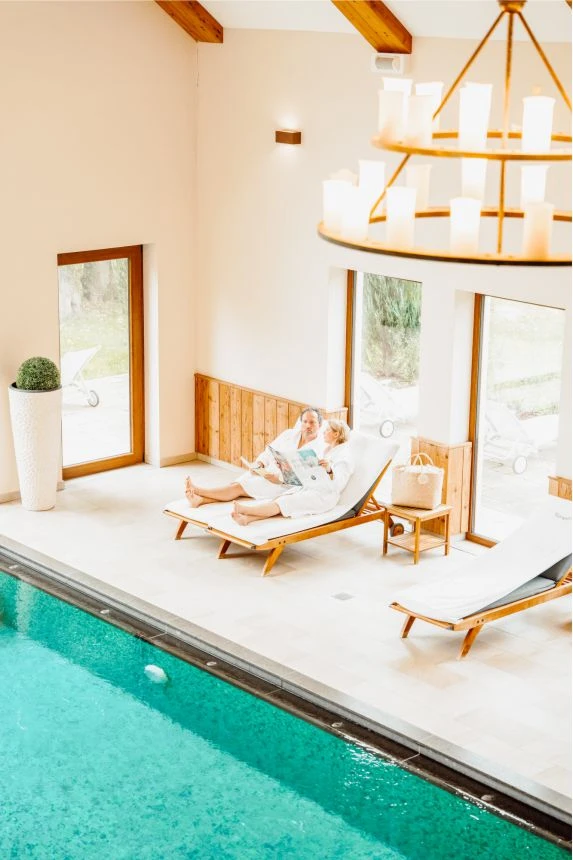 Blick von oben zum Paar am Pool auf Liegenstühlen mit Zeitungen