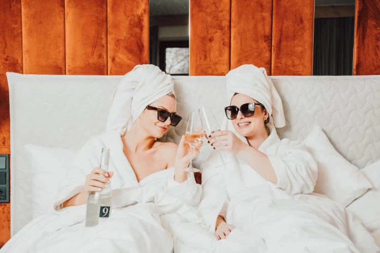 Zwei Freundinnen im Bett mit Bademantel, Turban und Sekt