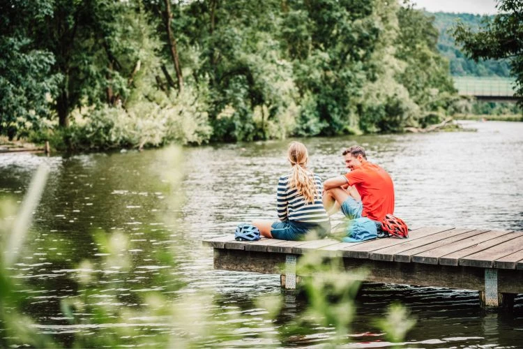 Wellnessurlaub für Zwei 10 Zwei Radfahrer sitzen an einem See am Steg