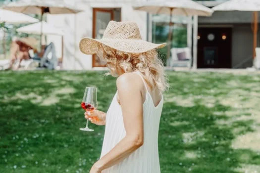 Frau im Kleid mit Strohhut und Glas Wein