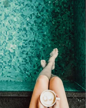 Single Wellness Urlaub 21 Frau sitzt am Poolrand mit Cappuccino und Beine im Wasser