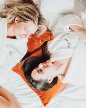 Zwei Freundinnen liegen Kopf am Kopf im Bademantel im Bett